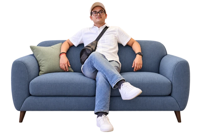A man seated on an illustrative blue-grey sofa with rounded arms and a sage cushion.